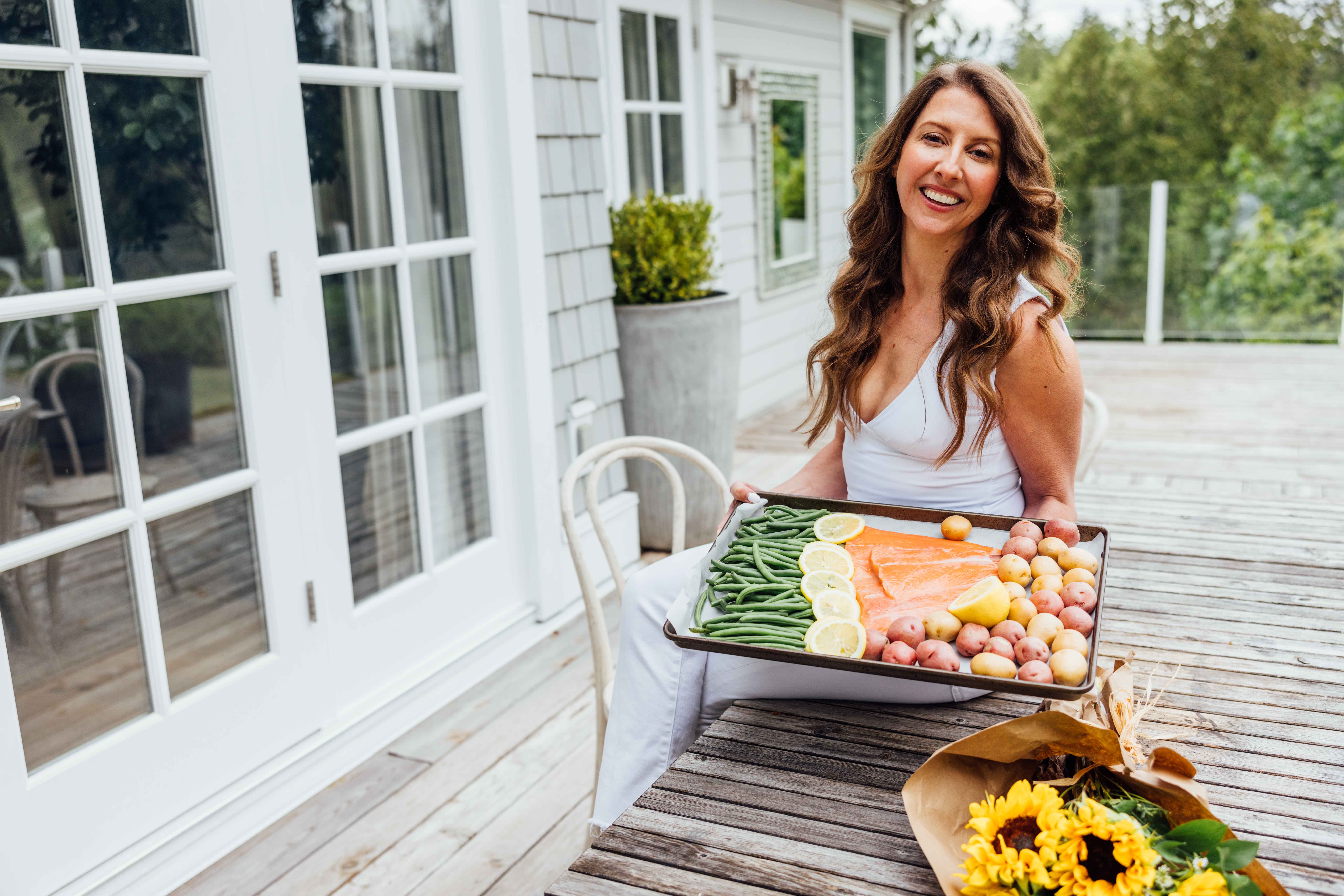 Simone Lovell seated on her porch with a sheet pan of salmon, green beans and potatoes